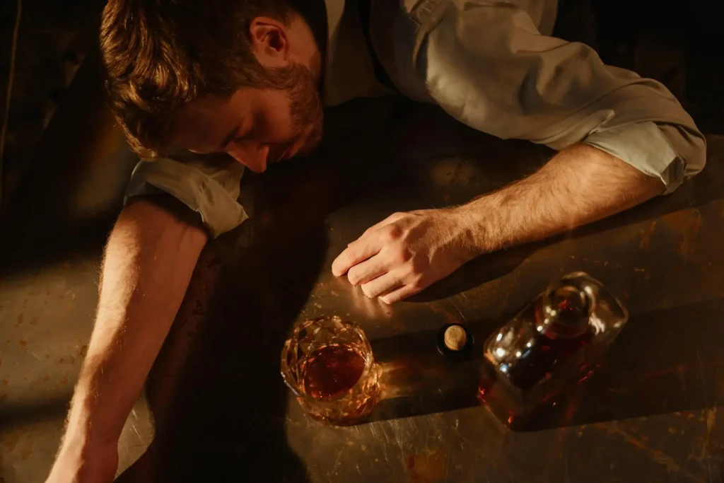 A man sleeping next to a glass and a bottle of alcohol